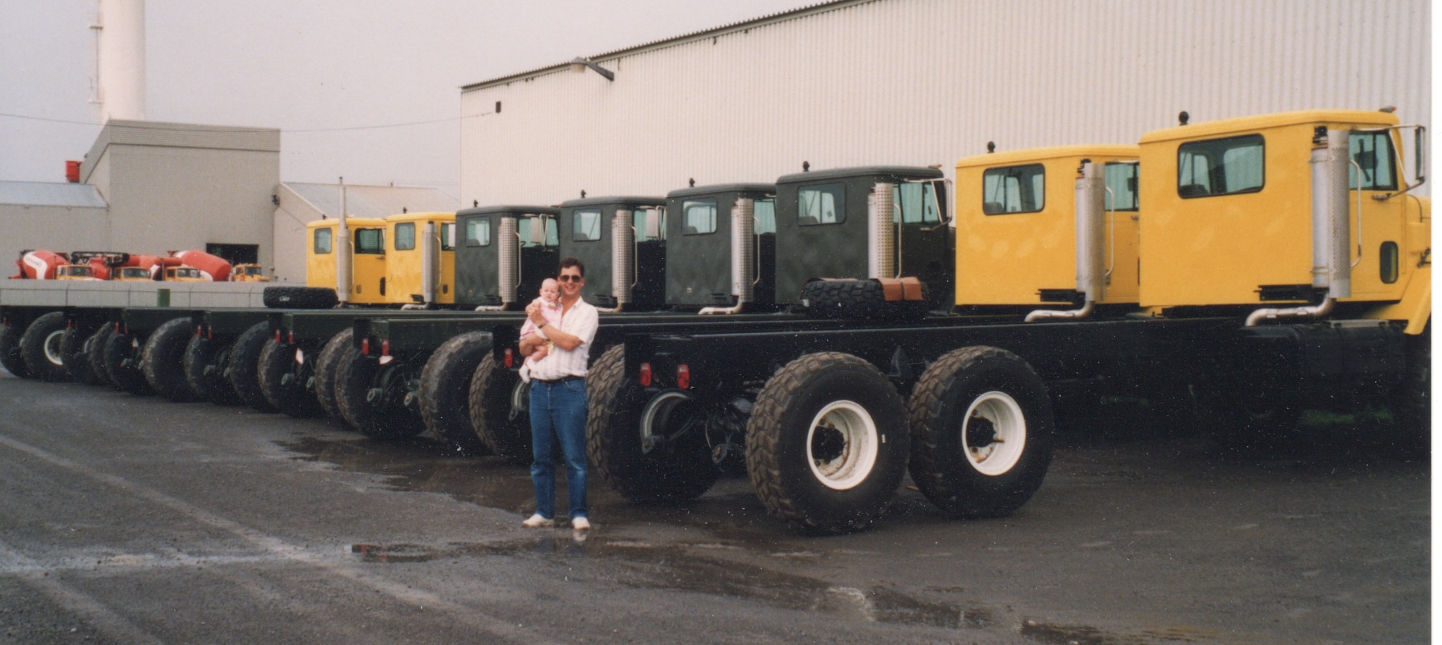 Luc Samson holding his baby daughter beside a lineup of trucks ready for Algeria in summer 1992